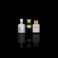 Three perfume bottles arranged side by side on a glossy black reflective surface against a black background. The left bottle is Crees Virgin Island Water clear glass with pale gold liquid and a white cap; the middle bottle is Sospiro Vibrato dark green glass with a gold cap and gold oval emblem; the right bottle is Nishbne hacivat white with a gold cap and the brand name NISHANE visible on the front.