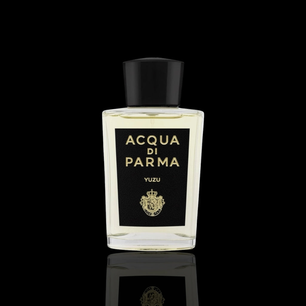 Acqua di Parma Yuzu bottle with clear glass, black label, and gold lettering on a black reflective background.