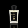 Acqua di Parma Yuzu bottle with clear glass, black label, and gold lettering on a black reflective background.